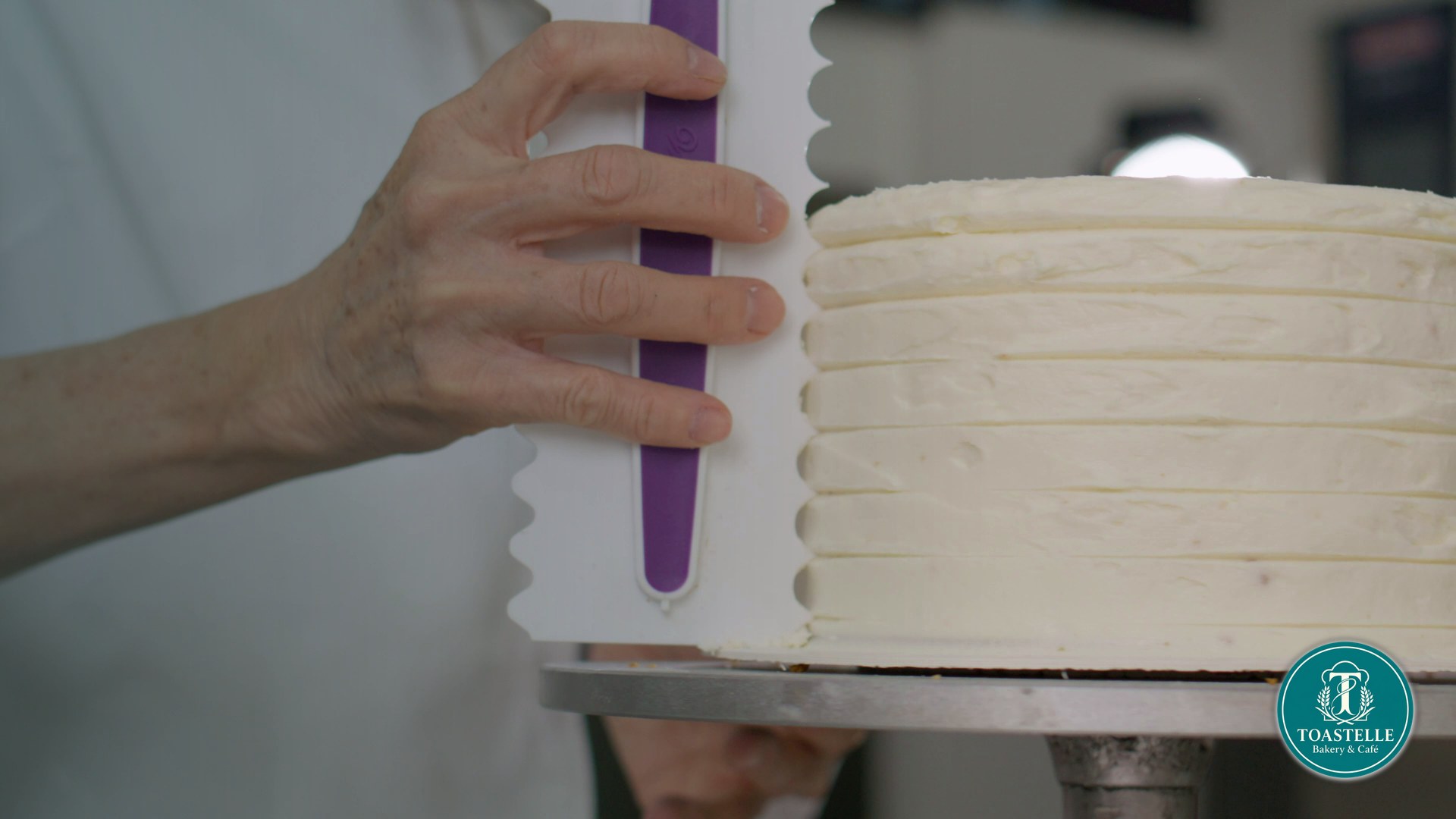 A cake being finished with a smooth layer of frosting